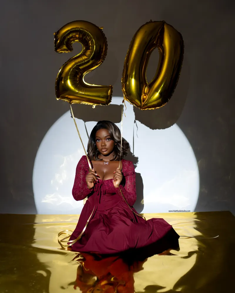 Same woman holding gold ribbon strings of the number-20 balloons floating above her head