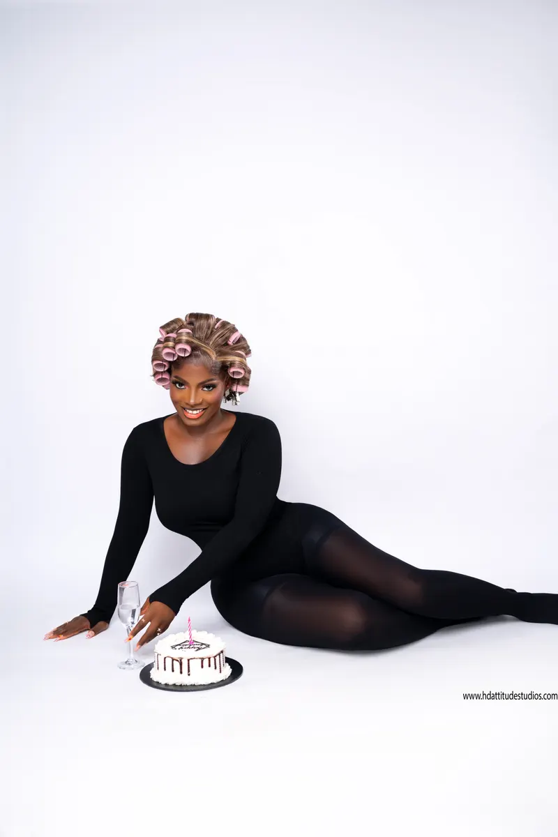 Seated in rollers beside a cake with candle and champagne flute