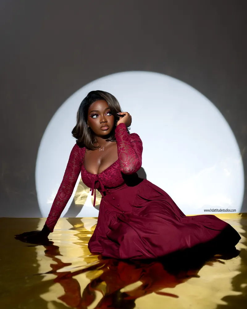 Solo woman in red lace gown lit by a circular spotlight against grey backdrop, gold reflective floor