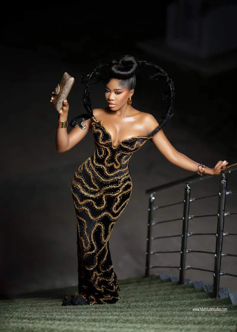 Same gown series, holding a gold clutch while leaning on railing at night