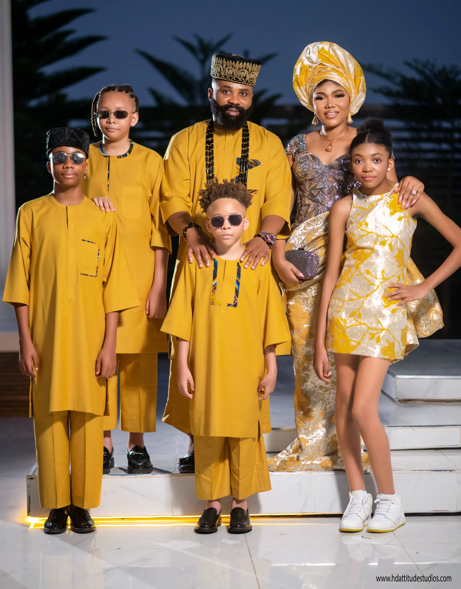 Full family of six in matching mustard-yellow aso-oke on an outdoor evening staircase