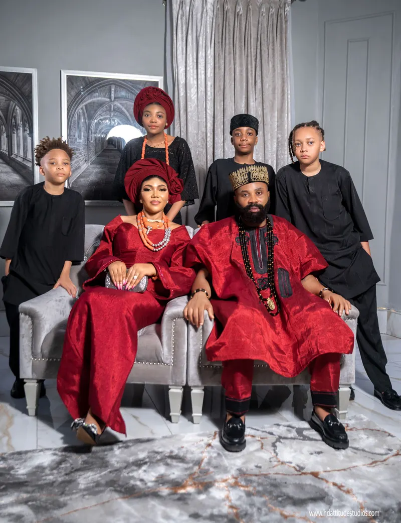 Family of six seated on a grey sofa in coordinated red and black traditional outfits
