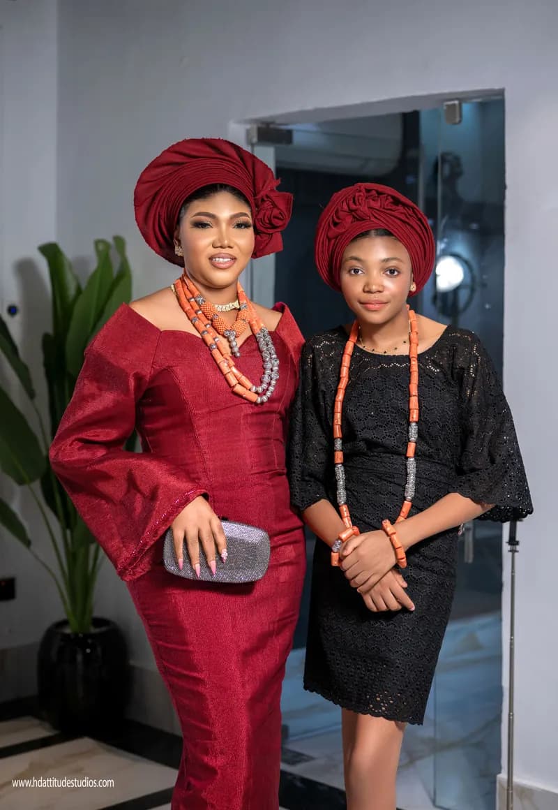 Mother and daughter in red and black with coral bead jewelry and matching gele/turban