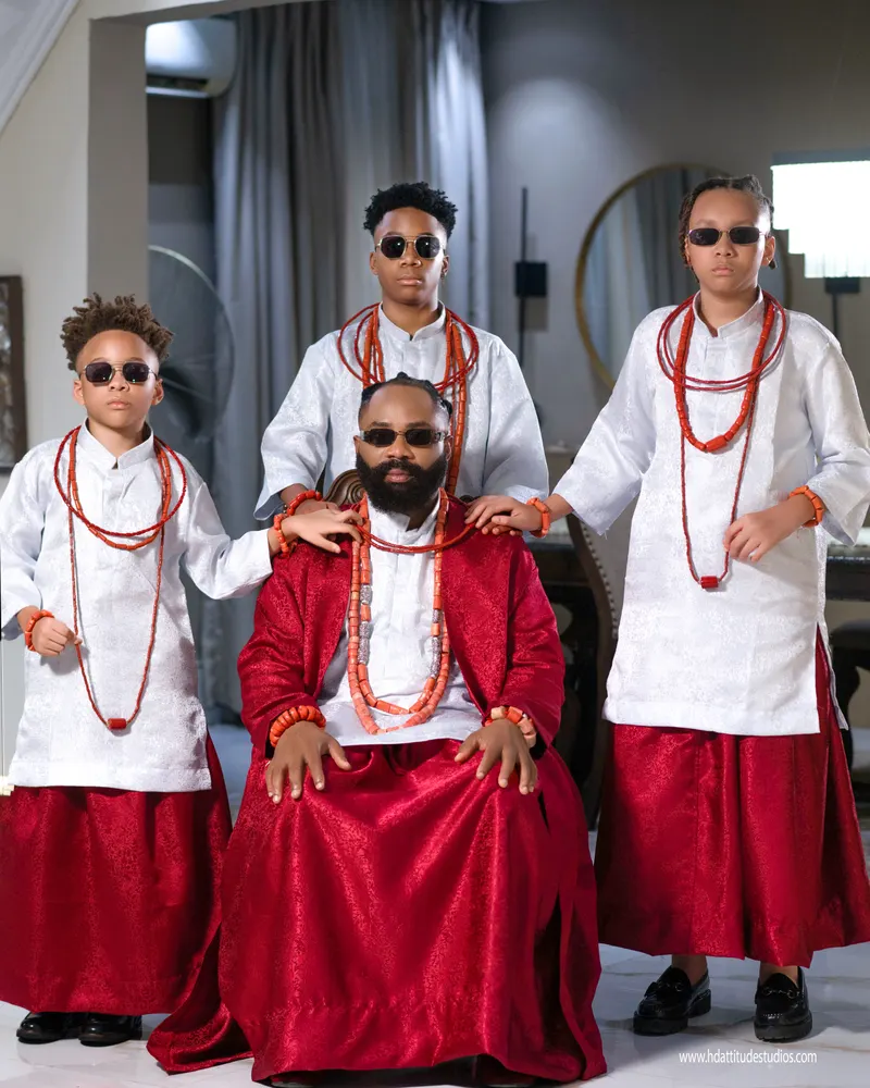 Father seated with three sons in red and white, coral beads, sunglasses