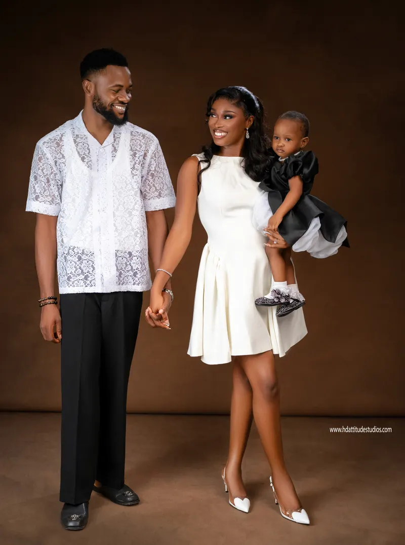 Young family portrait, parents in white/black with toddler in black satin dress, brown backdrop