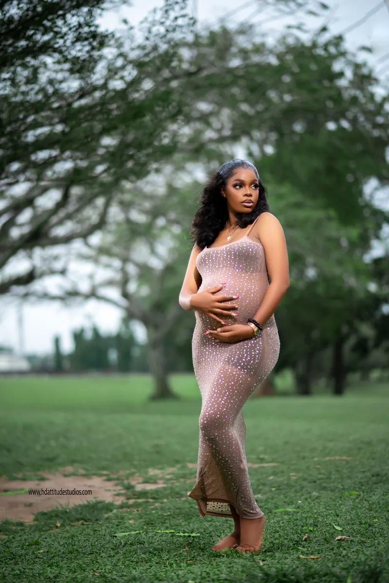 Maternity portrait outdoors in a sparkly nude gown among trees, natural light