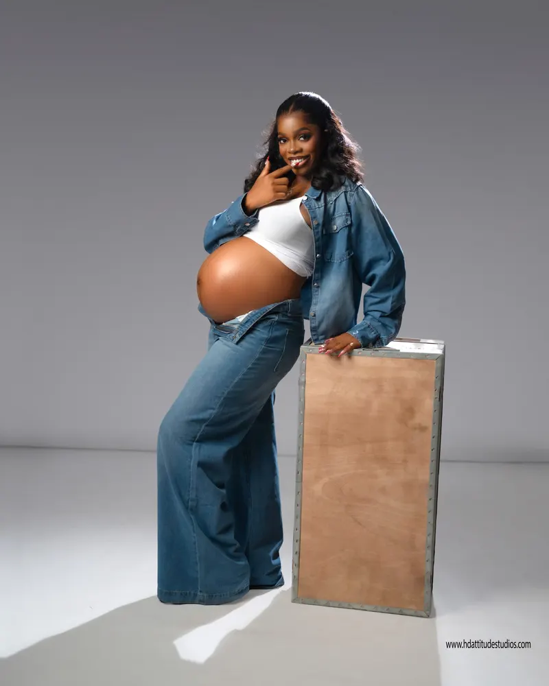 Studio maternity, denim jacket look, standing pose leaning on wooden crate prop
