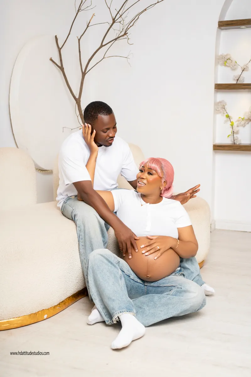 Maternity portrait, couple in white tees and jeans on a cream boucle sofa, white set