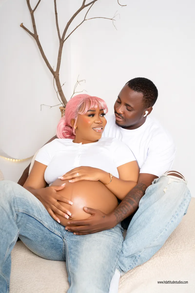 Maternity portrait, close embrace on the floor against the sofa, tender gaze