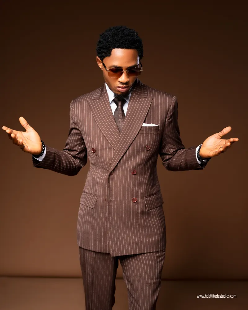 Man in brown pinstripe suit and sunglasses, plain brown backdrop, standing