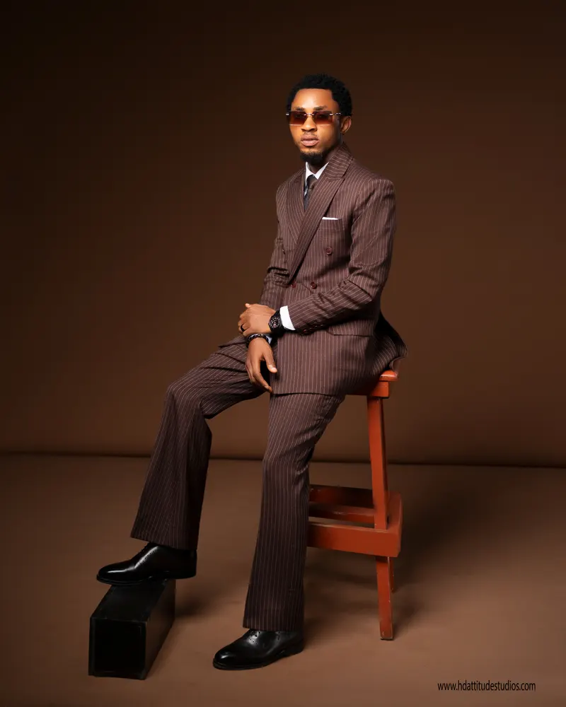 Same suit, seated on a stool with prop box, well-composed full body