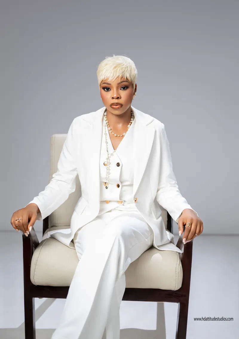 Same white suit set, seated in armchair, pearl necklace