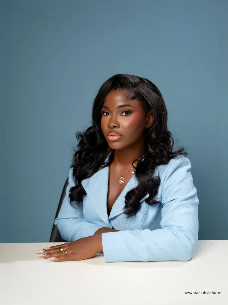 Corporate/personal-branding portrait, powder-blue blazer, seated at white desk on blue backdrop