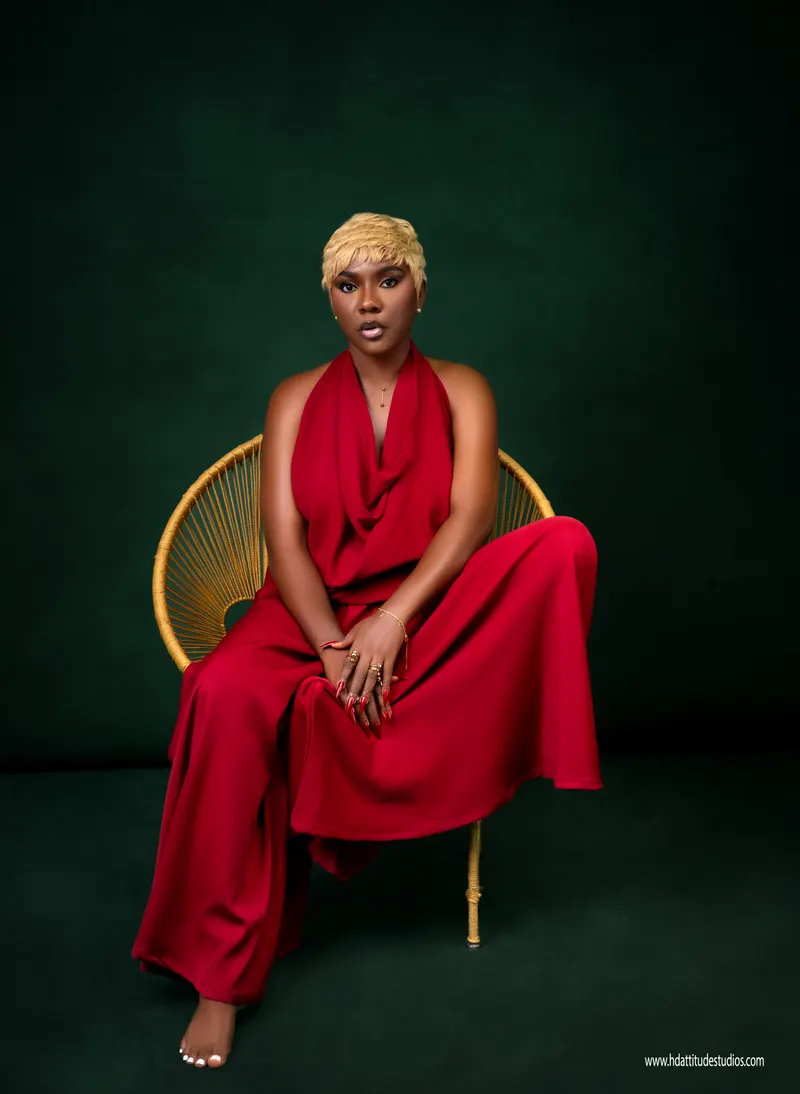 Glam seated portrait in flowing red halter jumpsuit on gold circular chair, green backdrop
