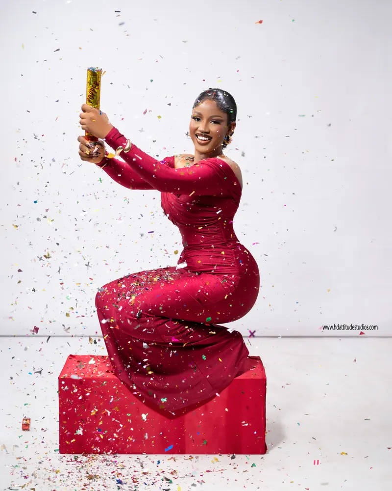 Confetti-popper explosion in a red gown atop a red pedestal box, festive