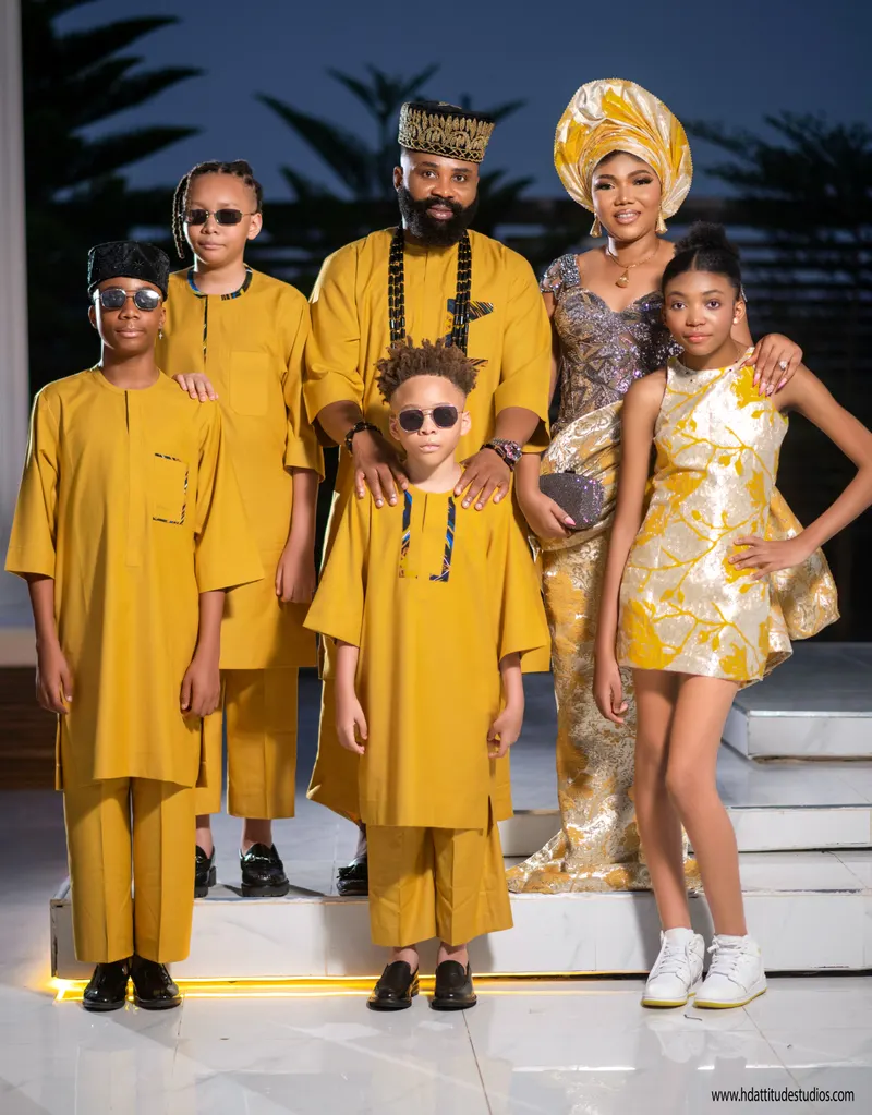 Full family of six in matching mustard-yellow aso-oke on an outdoor evening staircase