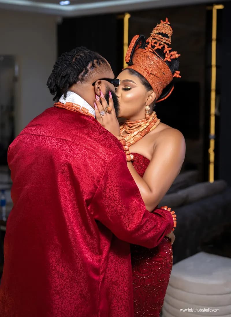 Intimate couple embrace/kiss moment in red traditional attire with coral crown